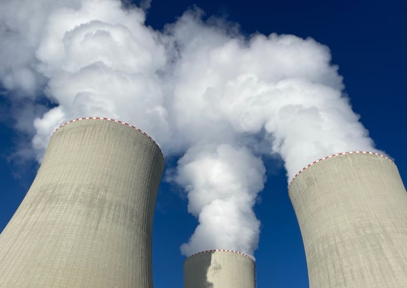 A photo of the cooling towers at the Temelin nuclear power plant in the Czech Republic. The towers are pictured against a bright blue sky, with steam emerging from them.