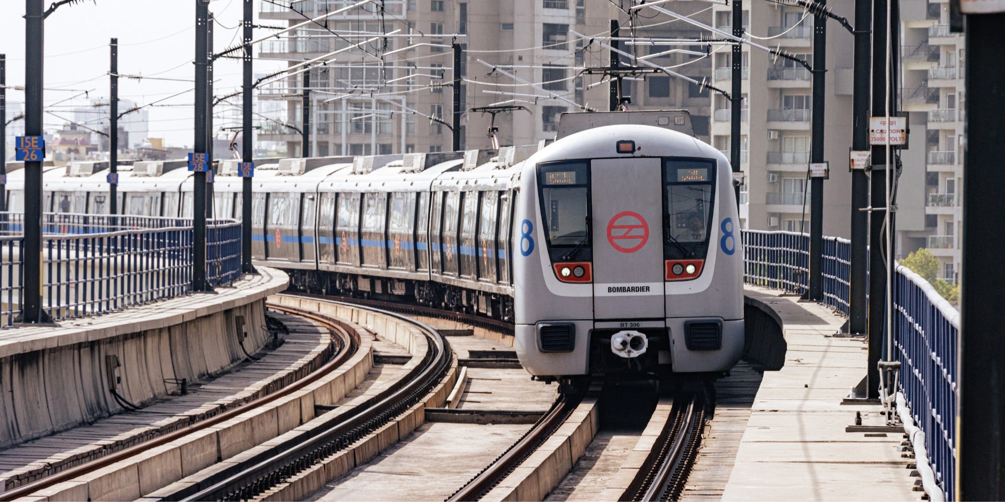 A photo of a Delhi metro grey train travelling on its rail lines. The photo looks at the train head-on.