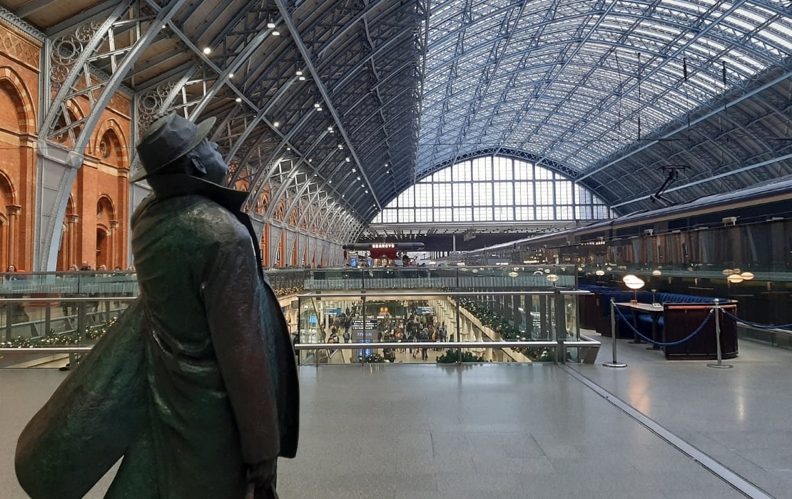 A photo of the interior of St Pancras International Station in London. There's a statue of man holding his hat in the foreground, facing away from the camera. The standout feature is the station's curved ceiling.