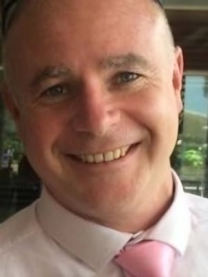 Close-up portrait of a person wearing a light-coloured shirt and pink tie, photographed indoors with a blurred background.