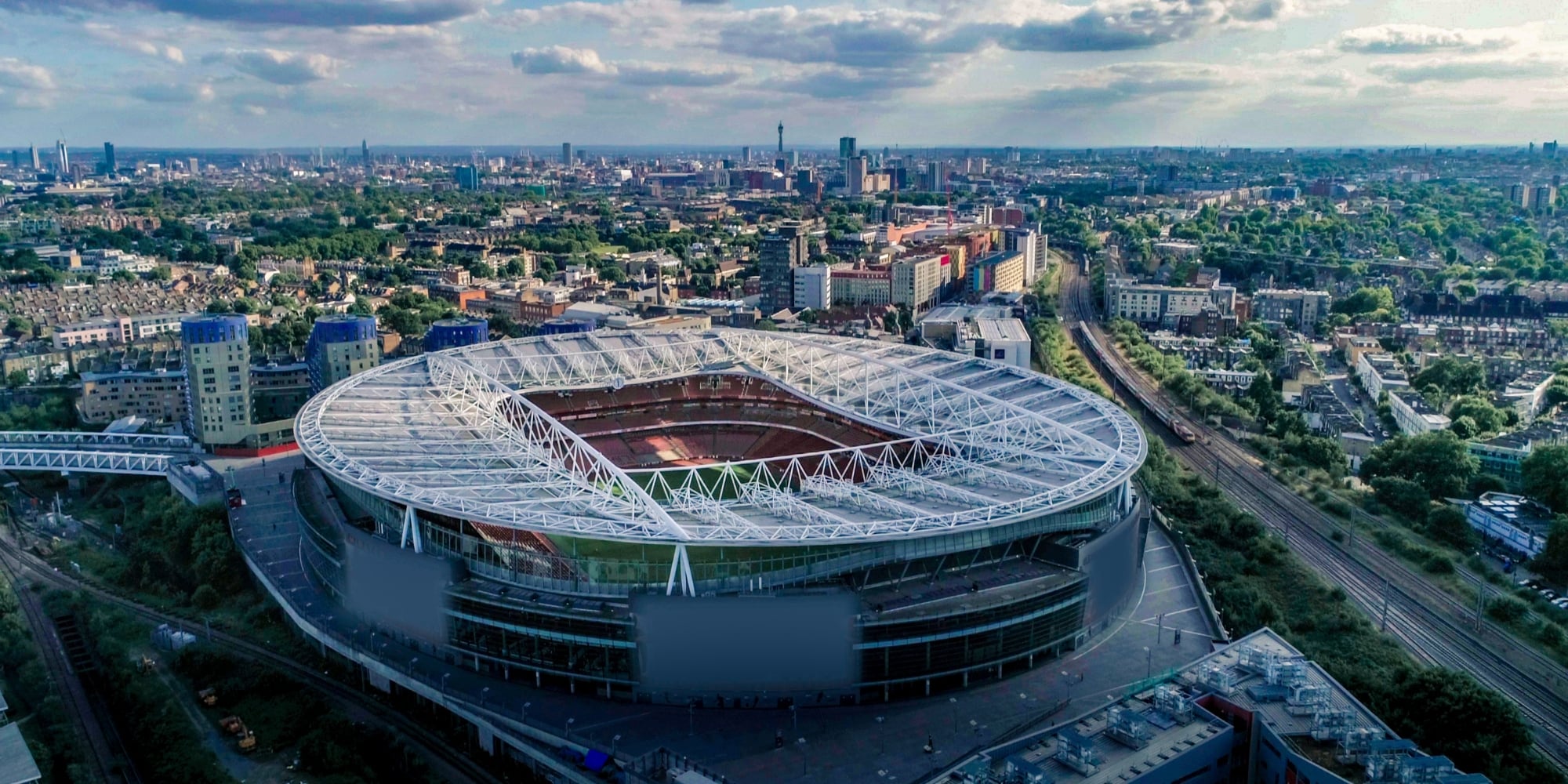 An aerial photo of the Emirates Stadium in north London, showing how the stadium was built in a dense urban area. The stadium is oval-shaped and it's a cloudy day.