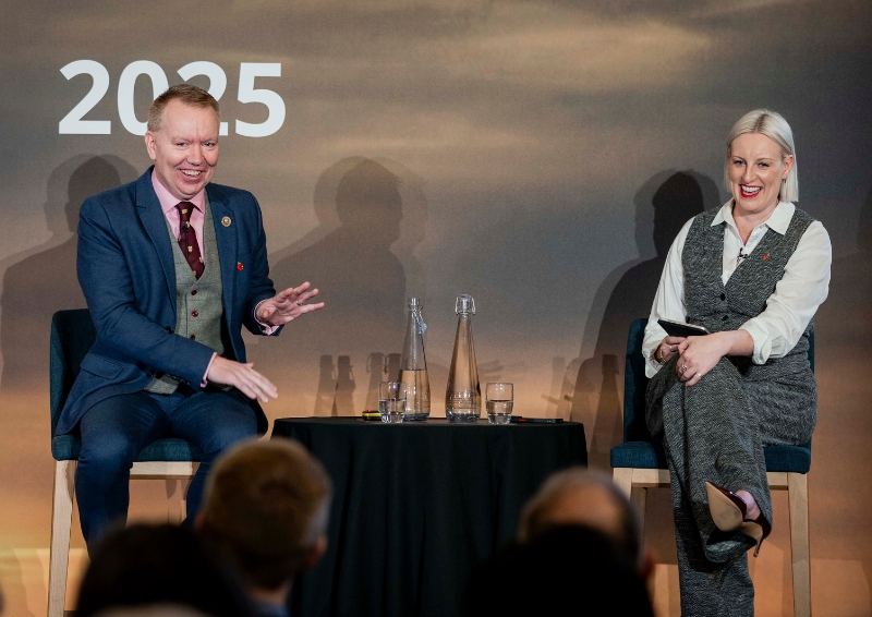 David Porter and Steph McGovern seated on stage in front of a backdrop that reads ‘Presidential Address 2025,’ with a small round table between them holding water bottles and glasses